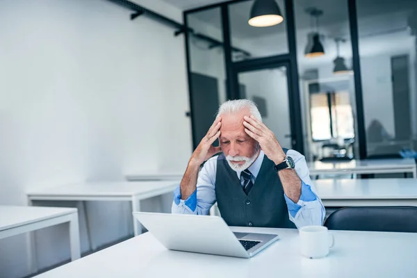 Worried senior business man holding head while looking at laptop.