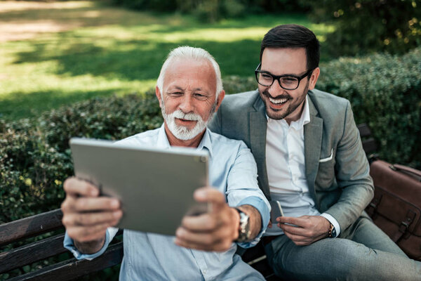 Two elegant men taking selfie on a tablet outdoors. 