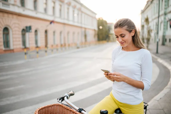 美丽的年轻女子在城市街道骑自行车时发短信 — 图库照片