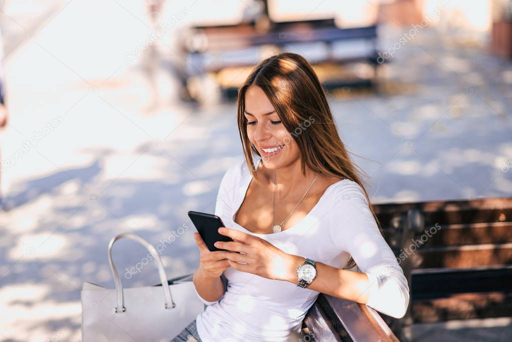 Attractive young woman texting while sitting on a bench.