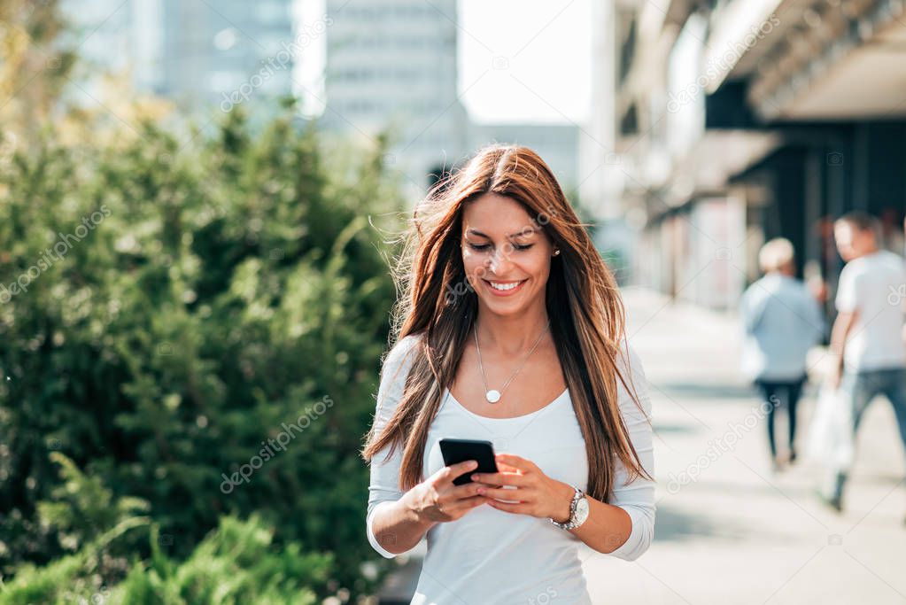 Young woman texting while walking in the city street.