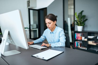 Modern ofis içinde bilgisayar üzerinde çalışan resmi kıyafeti içinde genç iş kadını.