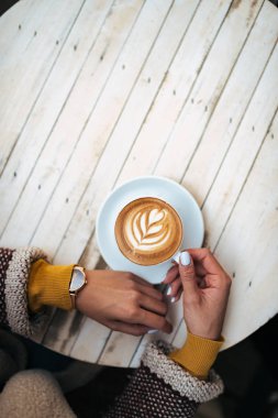 Bir fincan kahve latte sanat ile tutan genç kadın, üstten görünüm.