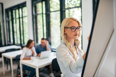 Flipchart üzerinde çalışan güzel bir genç kadın. Dizüstü bilgisayarda çalışma arka plan iş arkadaşları.