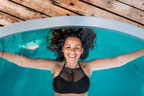 Close-up image of young woman with genuine smile floating in a swimming pool. Top view.