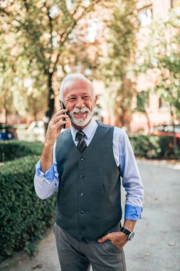 Açık havada akıllı telefonda konuşurken zarif olgun işadamı.