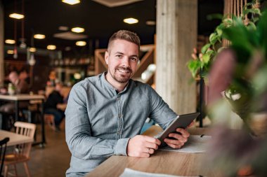 Modern bir kafede bir dijital tablet ile bir genç gülümseyen adam portresi.