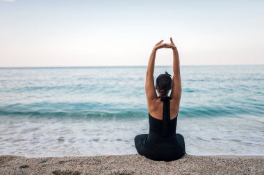 Ellerini uzanan kumsalda oturan genç kadın.