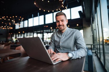 Modern restoranda dizüstü bilgisayar ile yakışıklı bir genç adam portresi.