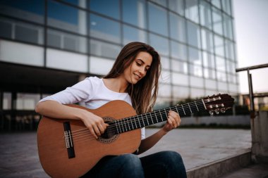 Güzel kız şehirde akustik gitar çalmak portresi.