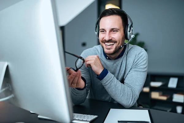Happy business man with headset at workplace in front of the computer.
