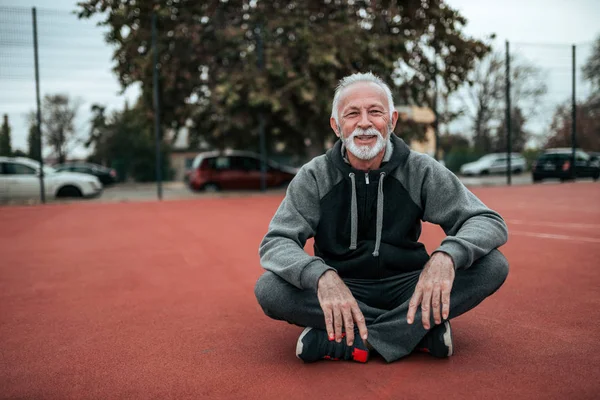 Portrait of a senior athlete sitting on the tartan track in outdoor stadium.