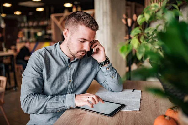 Young entrepreneur talking over mobile phone and using digital tablet.