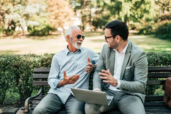 Two handsome business men talking while sitting on the bench.