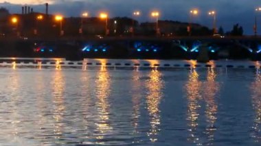 Nehirdeki bir gece şehrinin ışıklarının yansıması. Su yüzeyindeki köprünün çok renkli fenerlerinin yansıması..