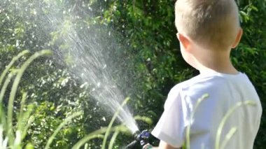 Bahçeyi hortumla sulayan genç bir çocuk.