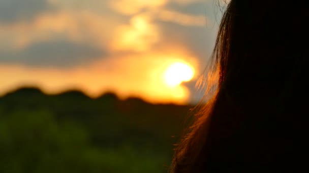 La fille à la fenêtre regarde le coucher du soleil et les nuages. Corrige les cheveux avec la main .