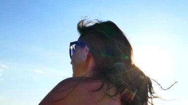 Güneş gözlüklü bir kızın portresi sahilde oturur ve gökyüzüne bakar..