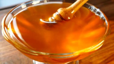 Bal, bal kaşığından tabağa dökülür. Taze sıkılmış bal güneşte parıldıyor.