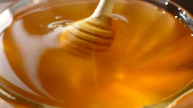 Bal, bal kaşığından tabağa dökülür. Taze sıkılmış bal güneşte parıldıyor.