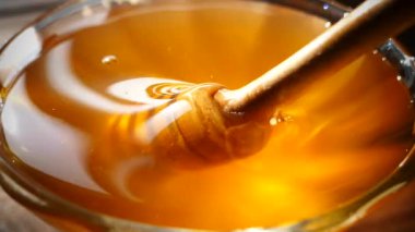 Bal, bal kaşığından tabağa dökülür. Taze sıkılmış bal güneşte parıldıyor.