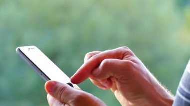 Onlar bir smartphone ellerinde tutmak ve doğa yeşil bir arka plan üzerinde bakmak. Telefonun dokunmatik ekran sayfalarında parmakları başparmak.