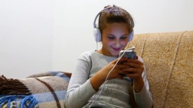 Kız gülümser, kulaklıkla akıllı telefona bakar ve müzik dinler..  