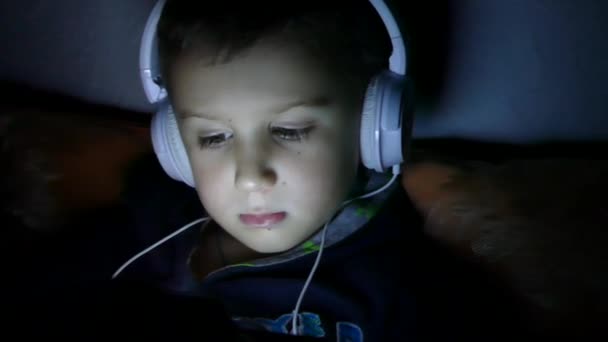 Anak Itu Melihat Tablet Headphone Ruangan Yang Gelap — Stok Video