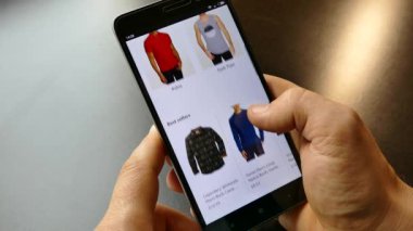 NEW YORK - 10 Aralık 2018: Akıllı telefondan online alışveriş. Elinde bir akıllı telefon ya da cihaz tut. İnternetten gömlek seç ve al. Mallar internetten alınıyor 
