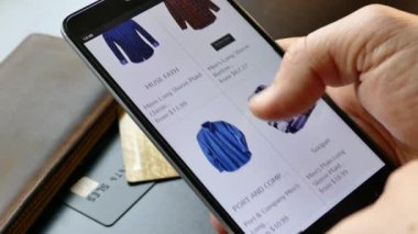 NEW YORK - 10 Aralık 2018: Akıllı telefondan online alışveriş. Elinde bir akıllı telefon ya da cihaz tut. İnternetten gömlek seç ve al. Mallar internetten alınıyor 