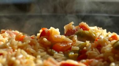 Büyük bir tavada pilav hazırla. Bir tabak pirinç ve sebze. Buhar sıcak bir öğle yemeğinden geliyor. Ev mutfağı. Pilaf ahşap bir spatulayla karıştırılır..