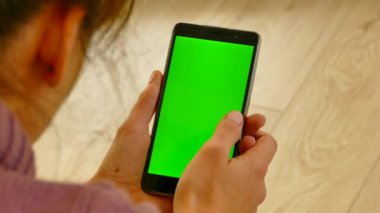 Akıllı telefon onların elinde tutulur ve onu kullanır. Yeşil arkaplanda yeşil ekran var. Kız aletimizin sayfalarını karıştırıyor. İnternetten alışveriş. Akıllı telefondan alışveriş yapmak. Krom