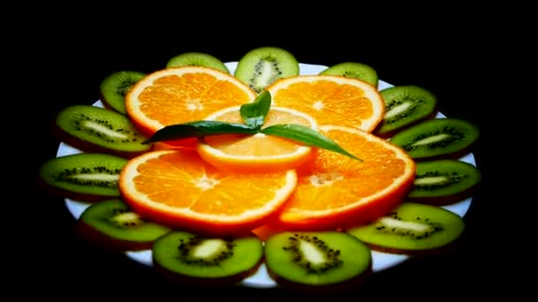 Tropikal meyve bir plaka üzerinde. Dilimlenmiş kivi portakal limon. Meyve siyah arka plan üzerine kapatın. Doğadan vitaminler. — Stok video