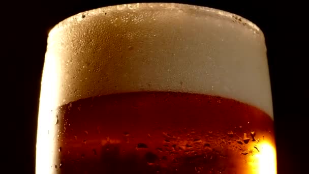 La birra con schiuma in un bicchiere gira su uno sfondo nero . — Video Stock