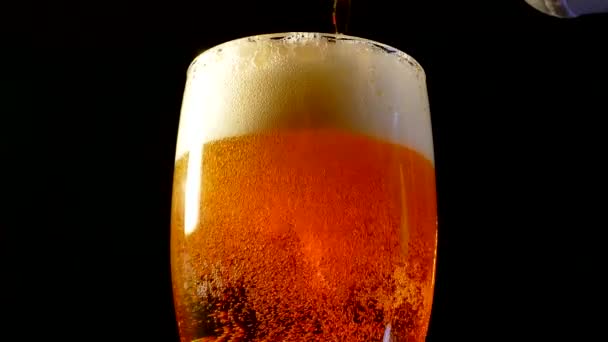 La bière avec de la mousse dans un verre tourne sur un fond noir . — Video