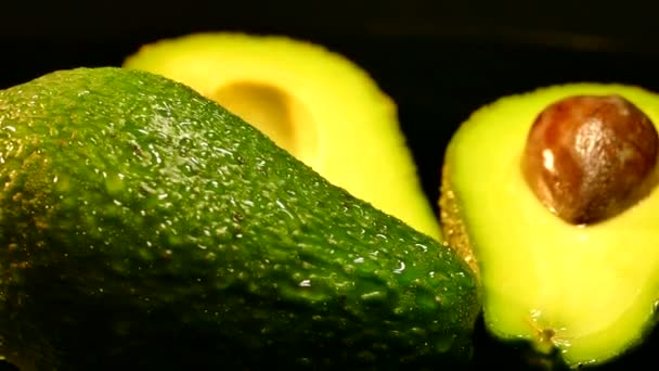 Aguacate de fruta madura sobre fondo negro. Comida sana y saludable. Cáscara verde, pulpa amarilla y tuerca grande . — Vídeos de Stock