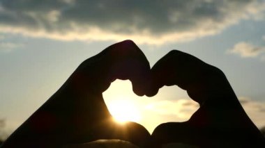 Ellerin kalbi. Gün batımında güneş ışınları kalp katlanmış elleriyle parlıyor.