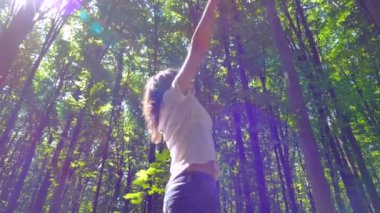 Güzel yeşil bir ormanda yürüyen bir kız. Summer Park 'ta. Kamp yapmak ve doğayla birlik olmak. Mutlu bir kız elleri havada ağaçların arasında dönüyor..