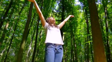 Güzel yeşil bir ormanda yürüyen bir kız. Summer Park 'ta. Kamp yapmak ve doğayla birlik olmak. Mutlu bir kız elleri havada ağaçların arasında dönüyor..