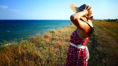 Kız sabahleyin güzel manzaraya bakıyor. Denizin kıyısındaki bir uçurumda dur. Tatilde şapkalı mutlu kız..