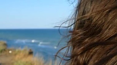 Saçlar rüzgarı sallıyor. Kız denizin yanındaki plajda duruyor. Dalgaların ve okyanusun arka planına karşı. 