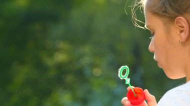 Genç bir kız sabun köpüğü üflüyor. Doğadaki mutlu çocuklar oynar. 