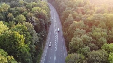 Ormanın içinden geçen yol. Gün batımında otoyol üst görünümü. Arabalar bir orman boyunca döşenmiş bir asfalt yol boyunca sürücü. Aero çekim izleri.