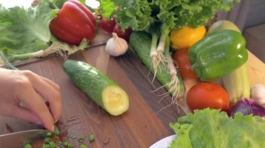 Kadın eli, kesme tahtasındaki mutfak bıçağıyla yeşil soğan kesti. Mutfak masasına bir tabak sebze koy. Salatalık domatesli lahana ahşap masada soğan salatası biberi. 