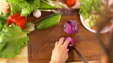 Kadın eli, kesme tahtasındaki mutfak bıçağıyla kırmızı soğanı kesti. Mutfak masasına bir tabak sebze koy. Domates salatalıklı lahana soğanlı salata biberi..  