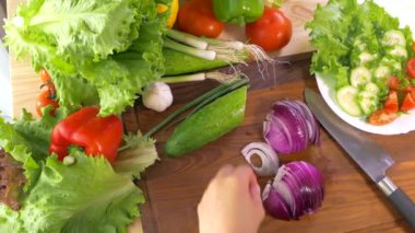 Kadın eli, kesme tahtasındaki mutfak bıçağıyla kırmızı soğanı kesti. Mutfak masasına bir tabak sebze koy. Domates salatalıklı lahana soğanlı salata biberi..  