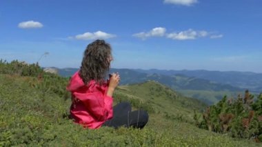 Dağların tepesindeki kız dinleniyor ve bir kupadan su içiyor. Şu güzel manzaraya bak. Dağlar, bulutlar ve orman. Yaz mevsimdir ve güzel havadır. Huzur içinde yat..