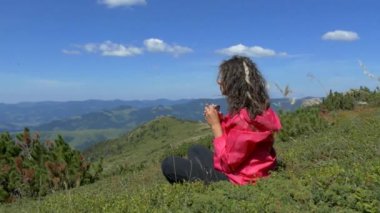 Dağların tepesindeki kız dinleniyor ve bir kupadan su içiyor. Şu güzel manzaraya bak. Dağlar, bulutlar ve orman. Yaz mevsimdir ve güzel havadır. Huzur içinde yat..