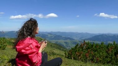 Dağların tepesindeki kız dinleniyor ve bir kupadan su içiyor. Şu güzel manzaraya bak. Dağlar, bulutlar ve orman. Yaz mevsimdir ve güzel havadır. Huzur içinde yat..