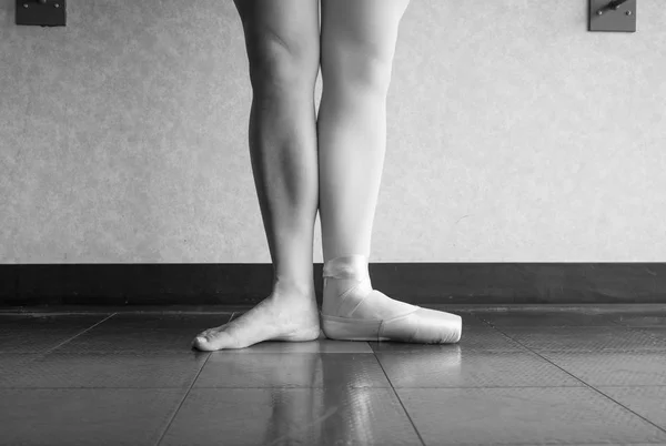 Black and white version of Two sides to a ballerina, one leg wearing her ballet slipper pointe shoe on one foot, and one leg bare